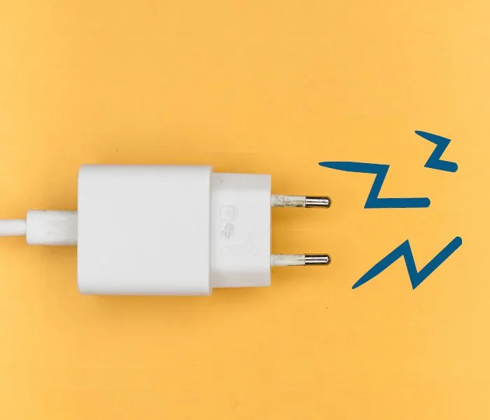 A white plug adapter with two metal prongs on an orange background with blue zigzag lines.