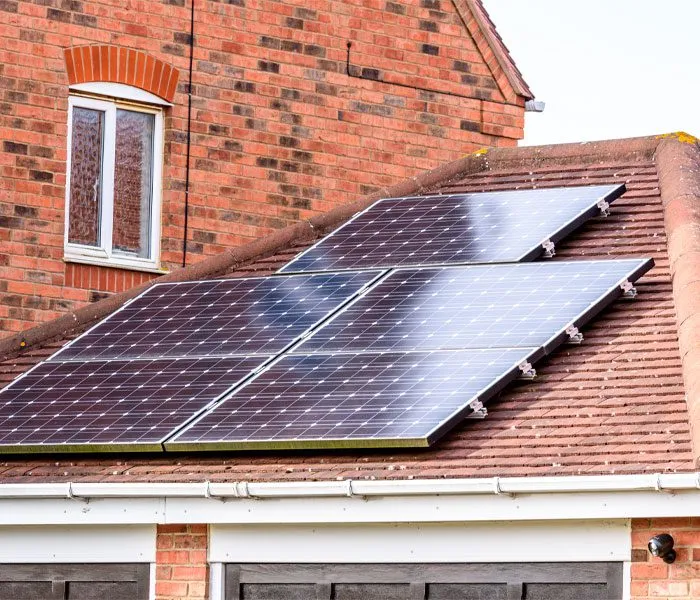 A residential roof with multiple solar panels installed, brick walls and a window in the background.