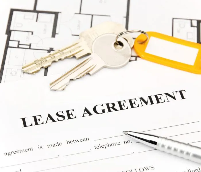 Lease agreement form with keys and a pen on a surface, placed over floor plans.