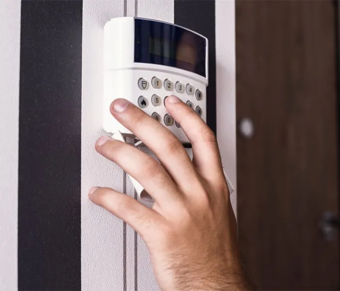 A hand entering a code on a wall-mounted keypad security system.